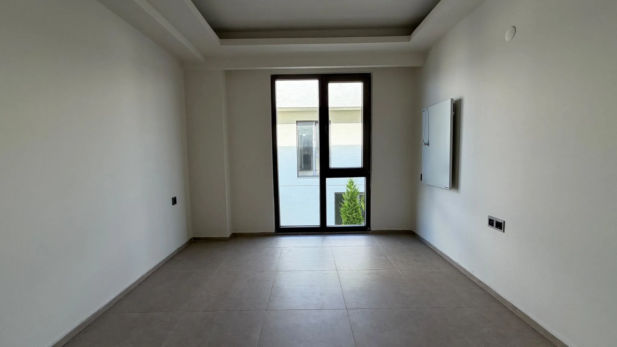 Empty room with a tall window and a recessed ceiling, photographed level so the walls stay straight